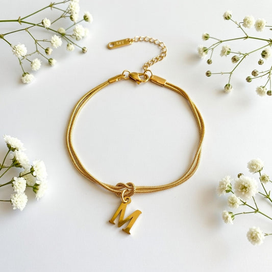 Gold bracelet with charm on a white background with small white flowers